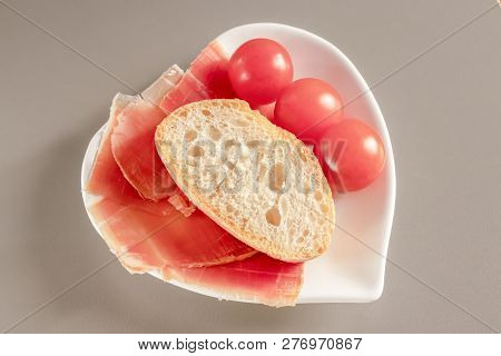 Dry Spanish Ham, Jamon, Italian Ham, Chopped Layers With Bread And Cherry Tomatoes On A White Heart-