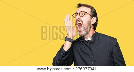 Middle age priest man wearing catholic robe shouting and screaming loud to side with hand on mouth. Communication concept.