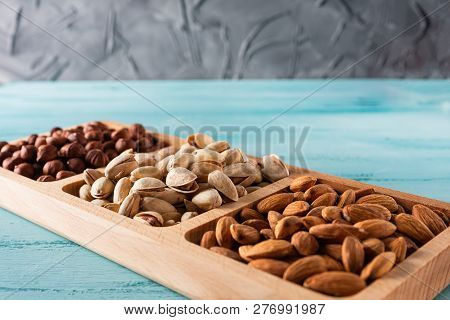 Compartmental Dish With Nuts On Blue Wooden Table. Hazelnut, Almond, Pistachio.