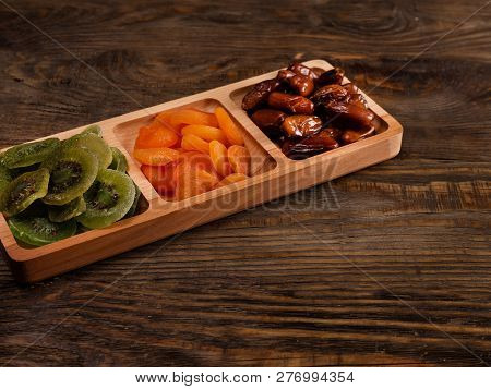 Dates, Dried Apricots And Kiwis In A Compartmental Dish On A Dark Wooden Table.