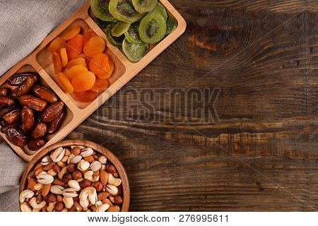 Dates, Dried Apricots And Kiwis In A Compartmental Dish And Assortment Of Nuts In Wooden Bowl On A D