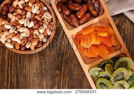 Dates, Dried Apricots And Kiwis In A Compartmental Dish And Assortment Of Nuts In Wooden Bowl On A D