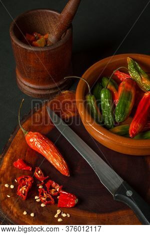 Still Life Of Hot Peppers In A Mortar Next To A Bowl And A Knife On A Dark Background
