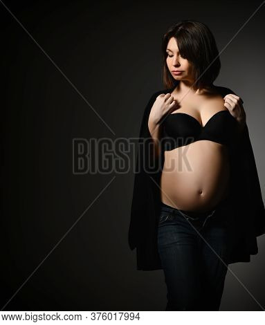 Brunette Pregnant Woman In Black Shawl, Pants And Bra, Bare Belly. She Looking Aside, Posing Sideway