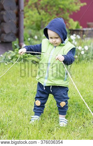 A Child Dressed In A Vest And Hoodie Stretches An Electric Wire Against A Background Of Greenery