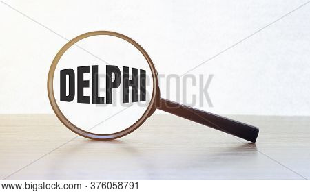 Magnifying Glass With Text Delphi On Wooden Table.
