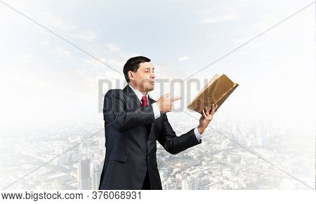 Senior Businessman Finger Pointing Into Open Old Book. Portrait Of Adult Man In Business Suit And Ti