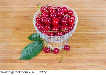 Freshly Picked Sour Cherries With The Leaves Of Cherry Tree In The Small Glass Cup On The Wooden Sur