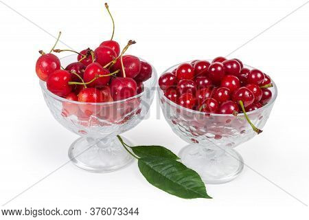 Fresh Sour Cherries And Sweet Cherries In The Two Glass Cups, Leaves Of Cherry Tree On A White Backg