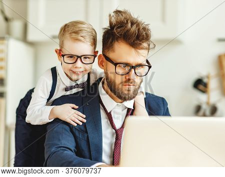 Concentrated Young Male Entrepreneur With Disarranged Hair And Cheerful Kid On Back Working On Busin