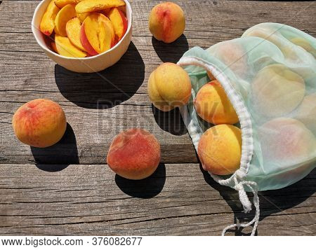 Juicy Sliced Peaches In A Plate, Whole Peaches And A Reusable Bag On Old Wooden Table. Bright Sun, H