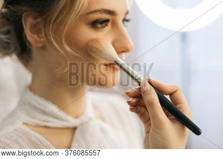 Close-up Of Make-up Artist Putting Rouge On Cheek Of Young Woman Using Brush While Hairdresser Makin