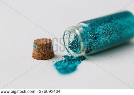party, decoration and holidays concept - close up of blue glitters poured from small glass bottle and cork stopper over white background