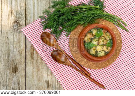 Delicious Soup With Croutons, Herbs In A Clay Pot On A Red Checkered Napkin. Pot With Broth And Dill