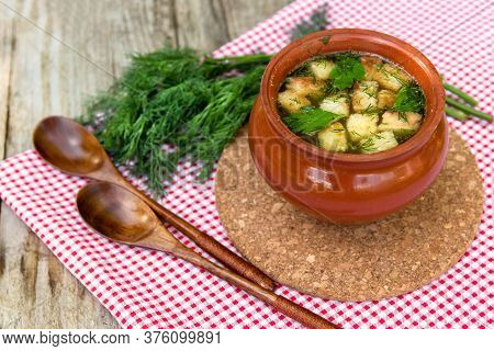 Delicious Soup With Croutons, Herbs In A Clay Pot On A Red Checkered Napkin. Pot With Broth And Dill