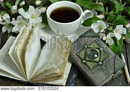 Open Diary Book With Cup Of Tea And Blooming Apple Tree Branches On Table. Esoteric, Gothic And Occu