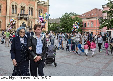 Novi Sad, Serbia - April 23, 2016: Two Old Women Passing By In Front Of A Crowd Of Kids And Young Ch