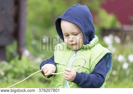 A Child Dressed In A Vest And Hoodie Plays With An Electric Wire Against The Background Of Nature