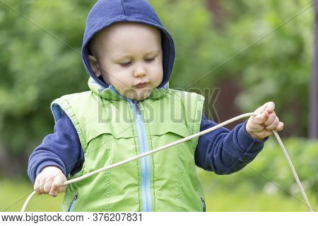 A Child Dressed In A Vest And Hoodie Plays With An Electric Wire Against The Background Of Nature
