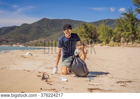 Man In Gloves Pick Up Plastic Bags That Pollute Sea. Problem Of Spilled Rubbish Trash Garbage On The