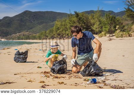 Dad And Son In Gloves Cleaning Up The Beach Pick Up Plastic Bags That Pollute Sea. Natural Education