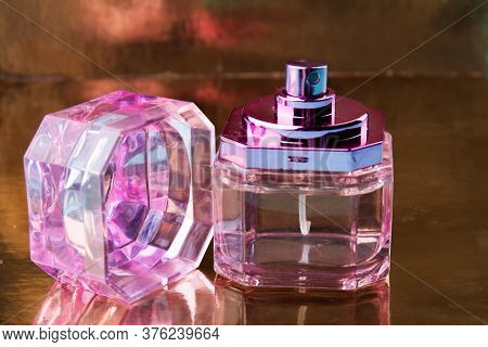 Pink Glass Perfume Bottle On A Reflecting Surface. Uncapped Perfume Bottle.