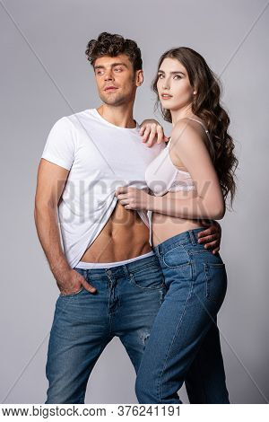 Attractive Woman Touching White T-shirt Of Handsome Boyfriend Standing With Hand In Pocket On Grey