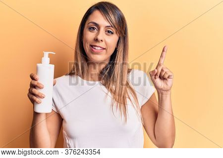Young beautiful woman holding bottle of cream lotion smiling happy pointing with hand and finger to the side 