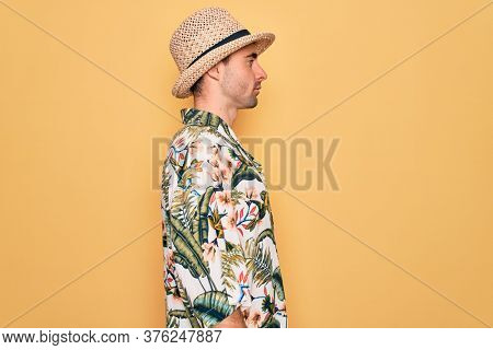 Young handsome man with blue eyes on vacation wearing summer florar shirt and hat looking to side, relax profile pose with natural face with confident smile.
