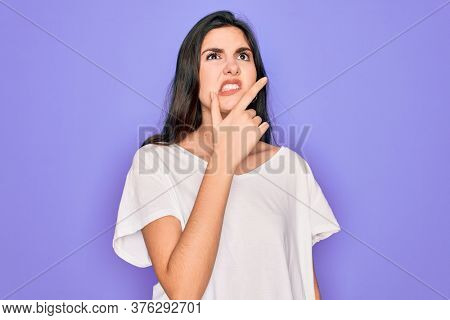 Young beautiful brunette woman wearing casual white t-shirt over purple background Thinking worried about a question, concerned and nervous with hand on chin
