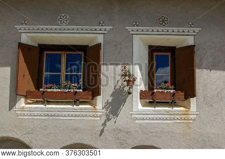 Two Windows With Wooden Shutters And Wall With Decorations, Village Of Zuoz, Tourist Resort In Engad