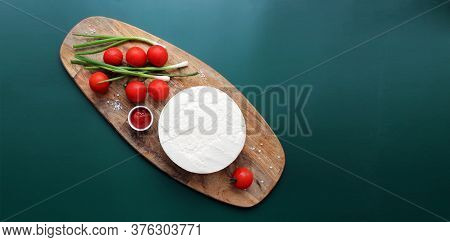 Homemade Goats Milk Cheese, Small Tomatoes On A Branch, Red Sauce On A Wooden Board On A Dark Green 
