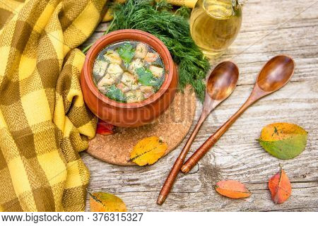 Autumn Transparent Soup With Croutons And Dill In A Clay Pot Against A Yellow Scarf, An Old Wooden B