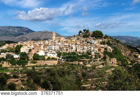 Sunny View Of The Hills Of Polop De Marina With Church And Castell Over Green Forest At The Costa Bl