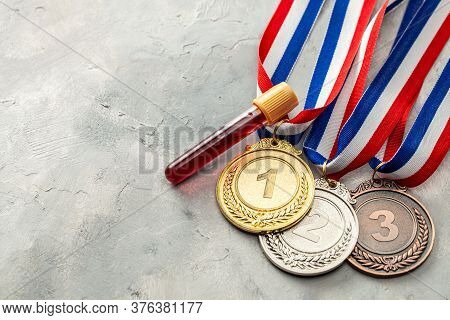 Doping Test. Gold, Silver And Bronze Medal And Test Tube With Blood On A Gray Background