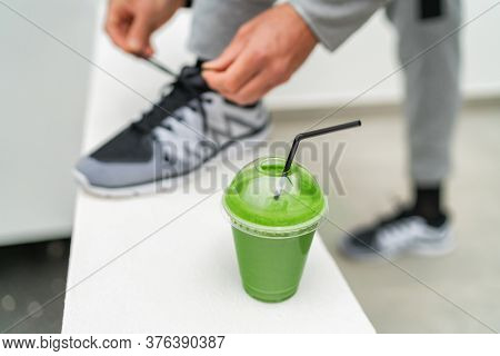 Healthy green smoothie food for detox eating lifestyle fit athlete man getting ready tying running shoes laces for morning walk jog drinking juice vegan diet for weight loss man training run workout.