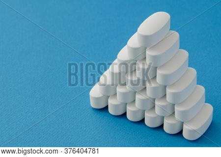 Pyramid From Many White Vitamin Drugs Medication Tablets On Blue Pure Surface With Copy Space