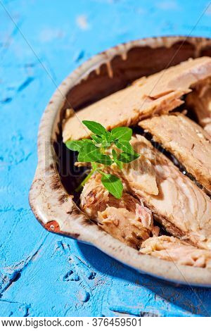closeup of some pieces of spanish bonito en aceite, a mackerel-like fish in oil, in an earthenware plate, on a textured blue surface