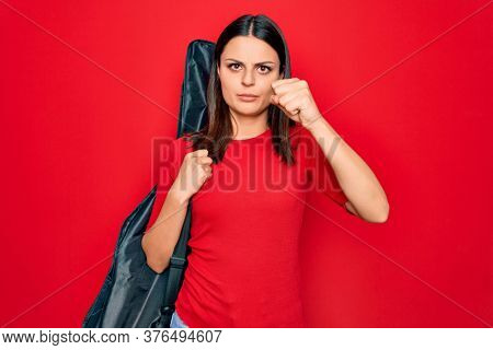 Young beautiful brunette guitarist woman holding guitar case over isolated red background annoyed and frustrated shouting with anger, yelling crazy with anger and hand raised