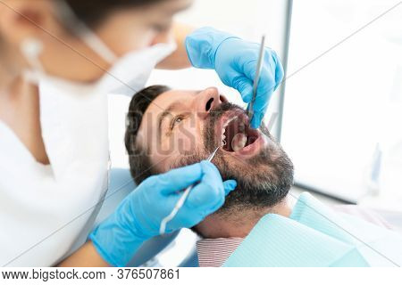 Female Odontologist Examining Patient With Mirror And Carver At Clinic