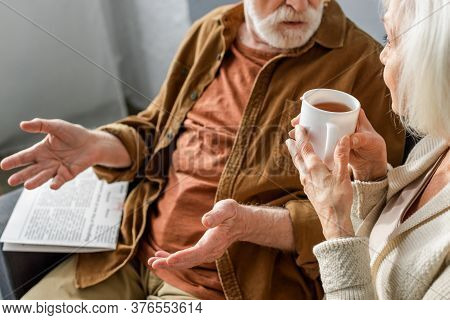 Cropped View Of Senior Man Showing Shrug Gesture While Talking To Woman Holding Cup Of Tea