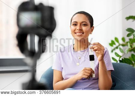 blogging, videoblog and people concept - happy smiling african american female video blogger with camera and smart watch videoblogging at home
