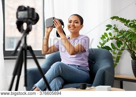 blogging, videoblog and people concept - happy smiling african american female video blogger with camera and vr glasses videoblogging at home