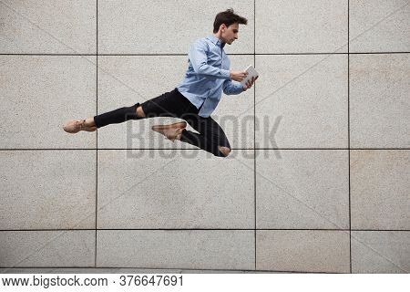 Jumping Young Buinessman In Front Of City Building Wall, On The Run In Jump High. Scrolling Tablet, 