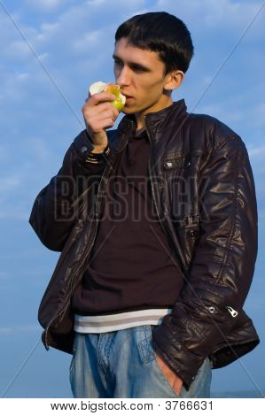 Jeune homme mange une pomme contre le ciel bleu et nuageux