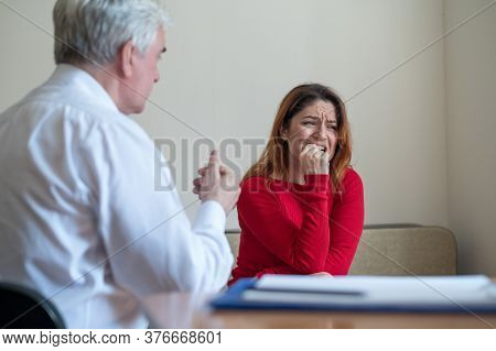 An Upset Woman Bites Her Nails At A Session With A Male Psychologist. Mature Gray-haired Psychothera