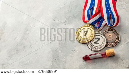 Doping Test. Gold, Silver And Bronze Medal And Test Tube With Blood On A Gray Background