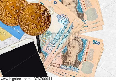 200 Ukrainian Hryvnias Bills And Golden Bitcoins With Smartphone And Credit Cards. Cryptocurrency In