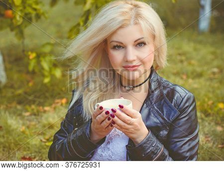Middle Age Stylish Blonde Hair Pretty Woman Dressed In Leather Black Jacket  In Autumn Garden With P