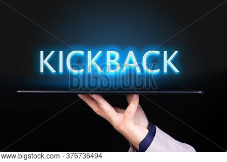 Man Hand Holds A Tablet Over Which A Neon Text Is Written, The Word Kickback. Business Concept.